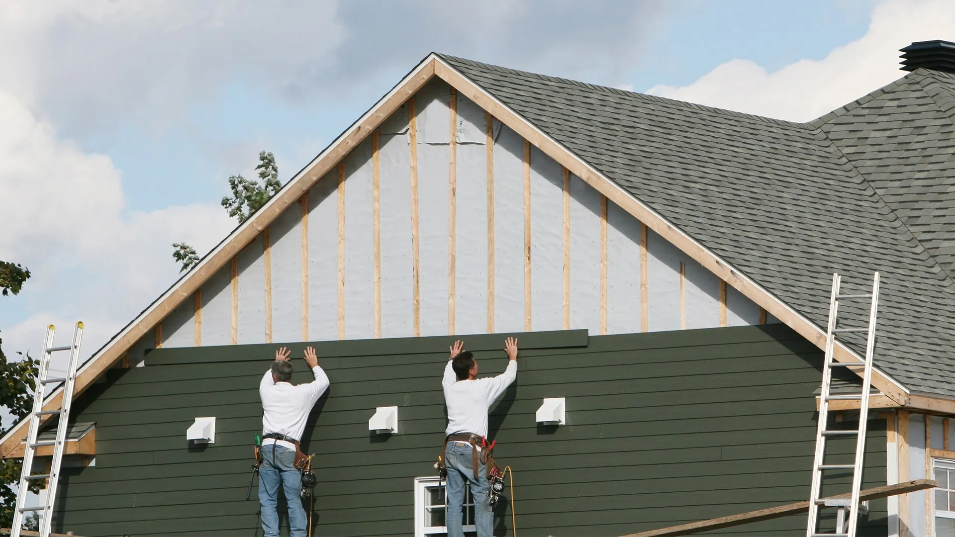 Professional crew installing modern fiber cement and insulated vinyl siding on residential home